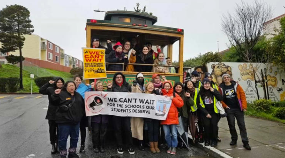 Group of educators standing in front of a trolley holding a banner that reads We Can't Wait.